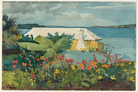 A garden of red and orange flowers beside a white bungalow and turquoise water