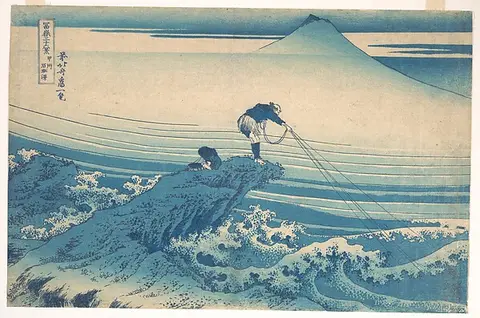 A fisherman on a rock pulling a line amid blue waves with Mount Fuji behind