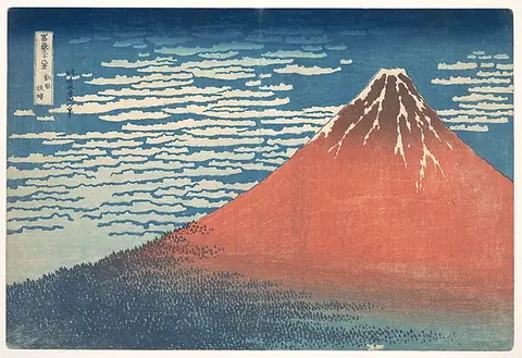 A red Mount Fuji against a deep blue sky streaked with white clouds