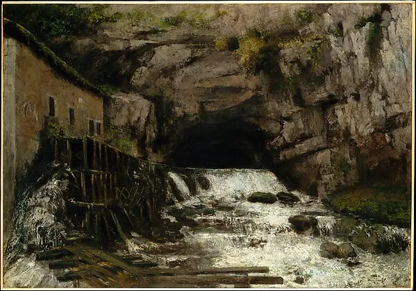 Water rushing from a cave in a rocky cliff beside an old wooden mill