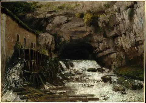 Water rushing from a cave in a rocky cliff beside an old wooden mill